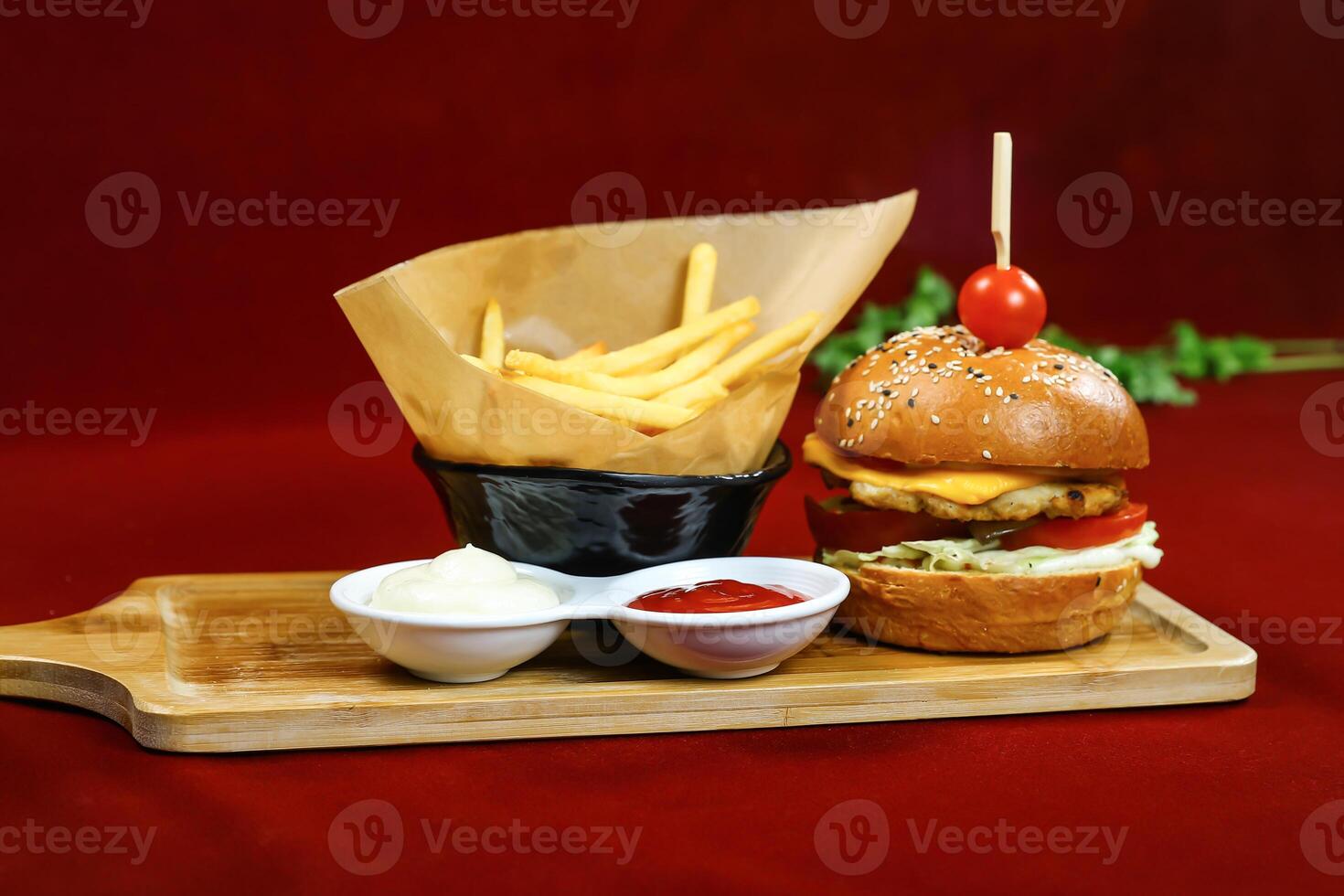 Chicken Burger and Fries topped with cheese, lettuce, and tomato served in wooden board with dipping sauce side view of fastfoods photo