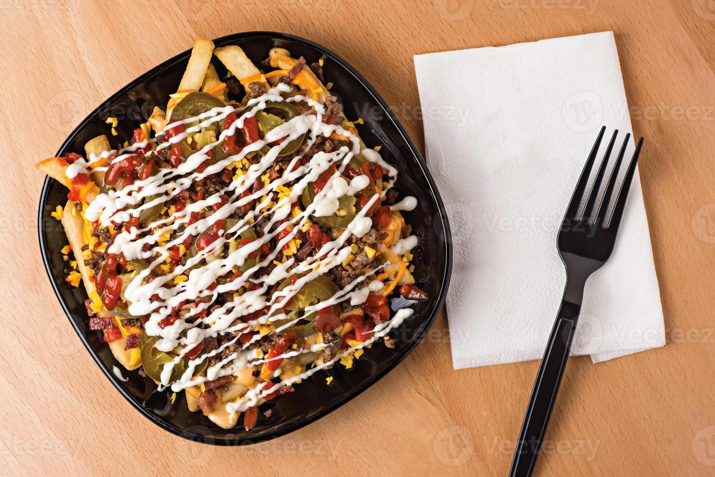Special Loaded Fries with Cheese, Bacon, Jalapenos, and Sauces served in plate isolated on wooden table top view fast food snacks photo