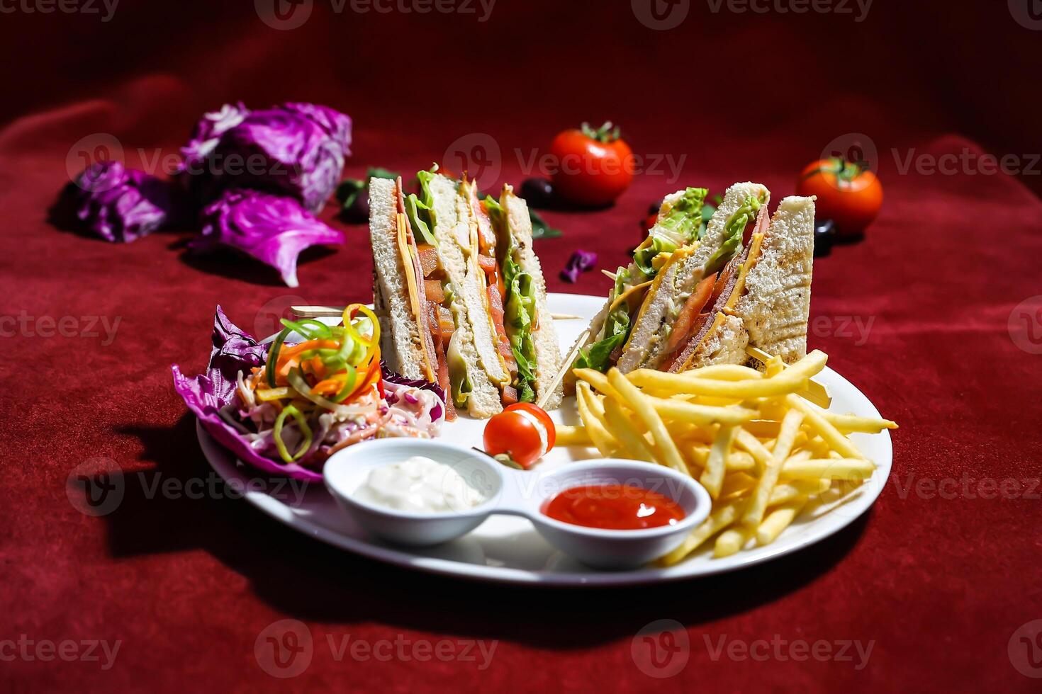 Classic Club Sandwich featuring layers of tender chicken, crispy bacon, cheese, lettuce, and tomato, served with a side of golden French fries, salad, ketchup and mayo sauce on red background photo