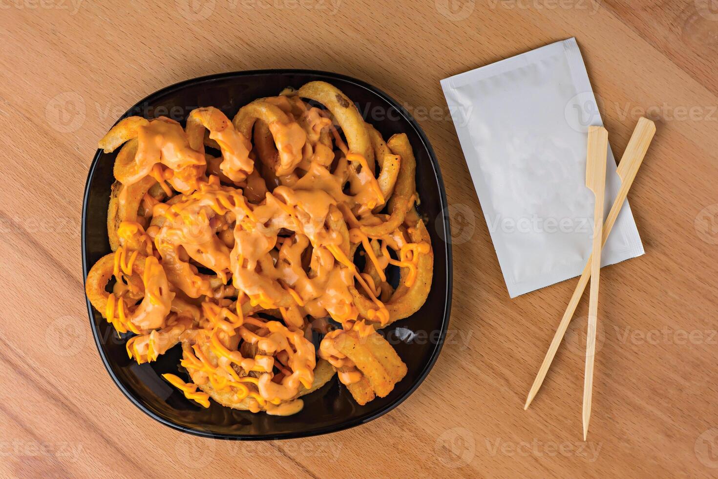Loaded Curly Fries with Cheesy Sauce and Dipping Sauce served in plate isolated on wooden table top view fast food snacks photo