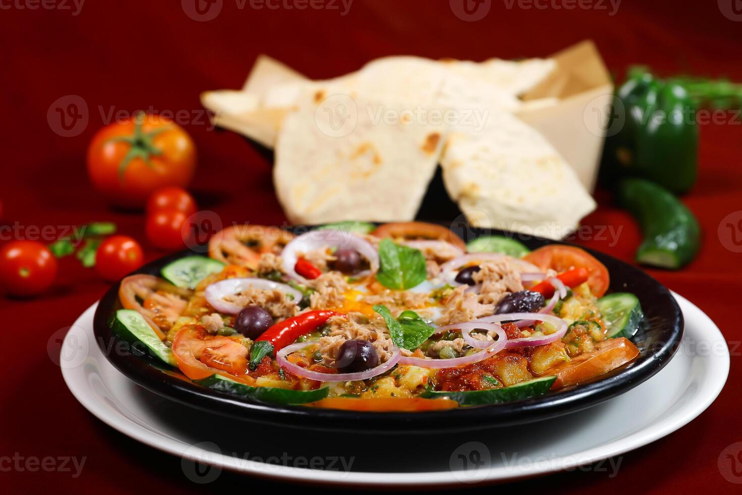 Colorful Tunisian Salad with Poached Eggs, mashed potatoes, cucumber, onion, mint, tomato, vegetables, poached eggs, and olives in plate isolated on red background side view of arabic food photo