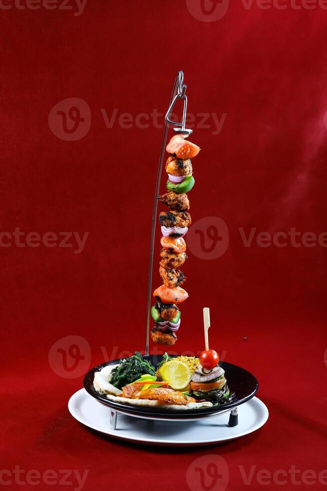 BBQ Chicken Shish tawook vertical skewer chicken tikka boti kabab with lemon, salad and biryani rice served in dish isolated on red background side view of arabic barbequed food photo
