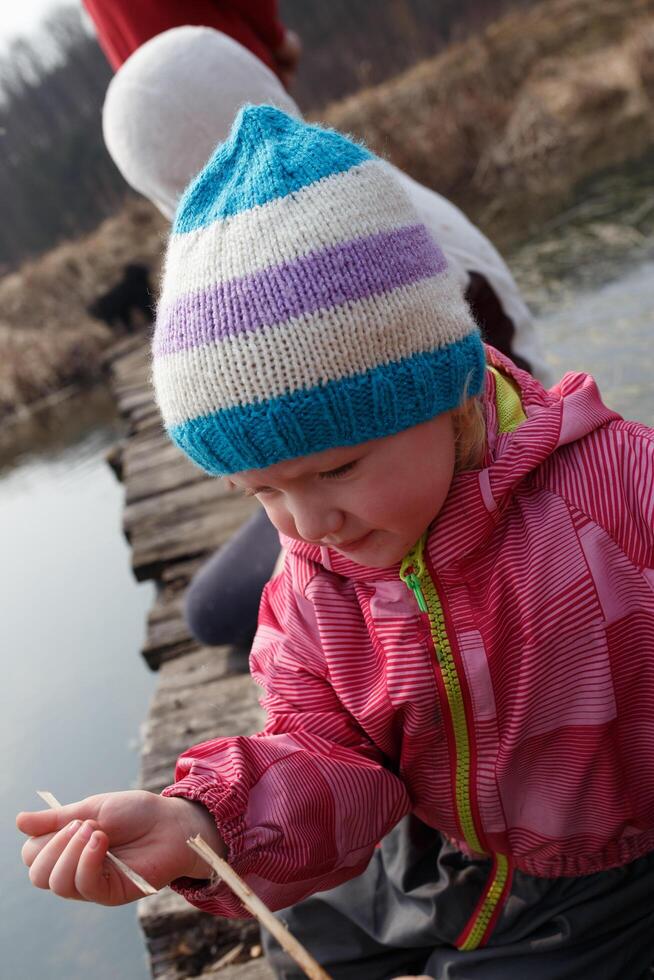Young child with colorful hat fishing along the water's edge on a sunny day in early spring photo