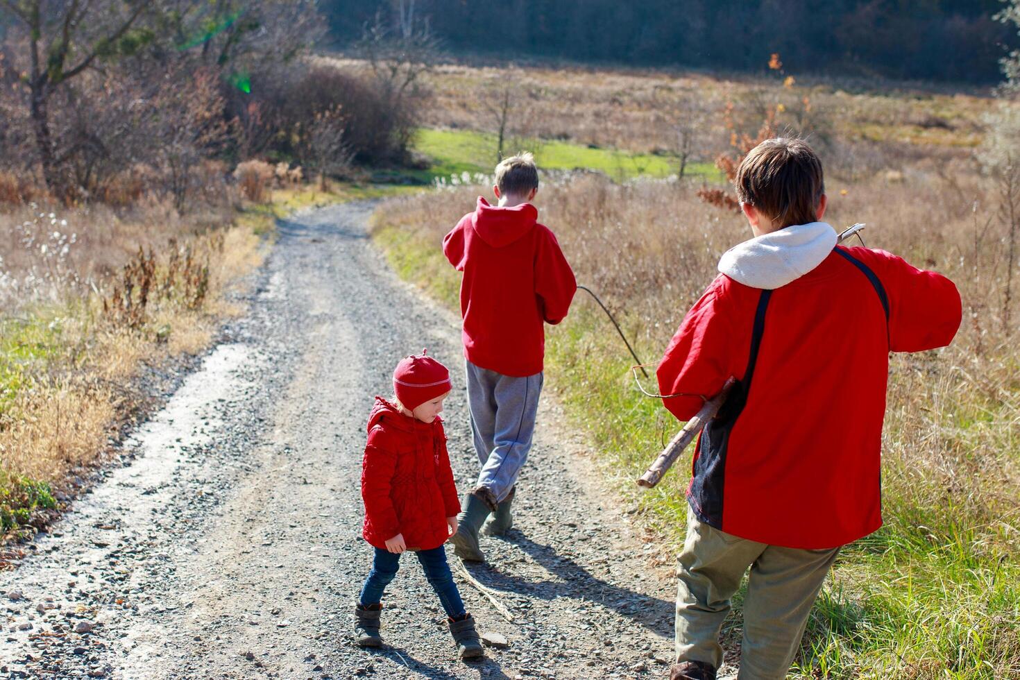 Children exploring a sunny trail in nature wearing bright red jackets on a cool autumn day with fields in the background photo