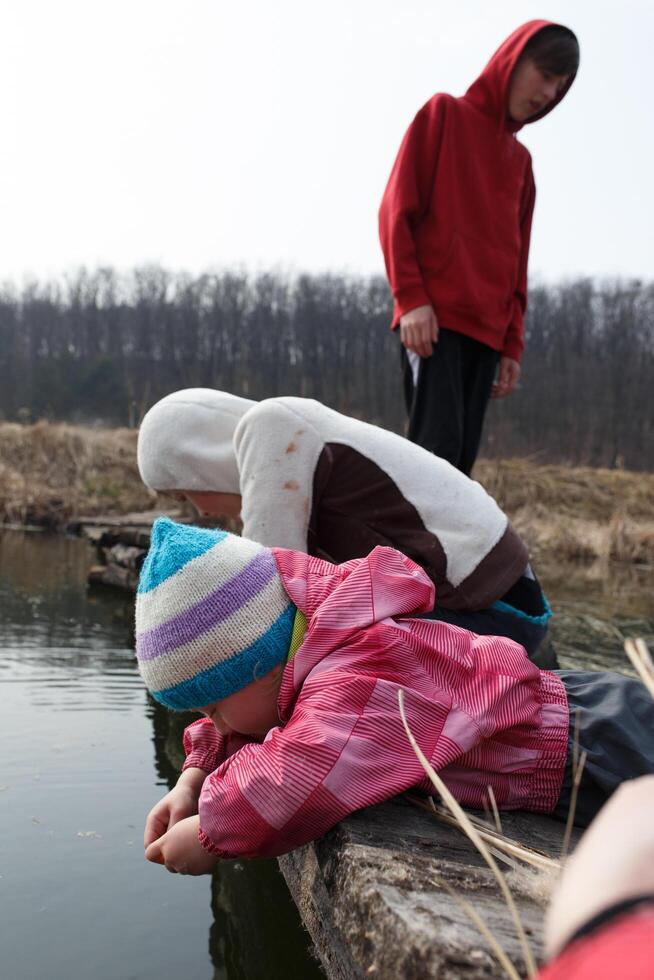 Children exploring the calm water on a chilly day, enjoying nature and playfully interacting with their surroundings in early spring photo
