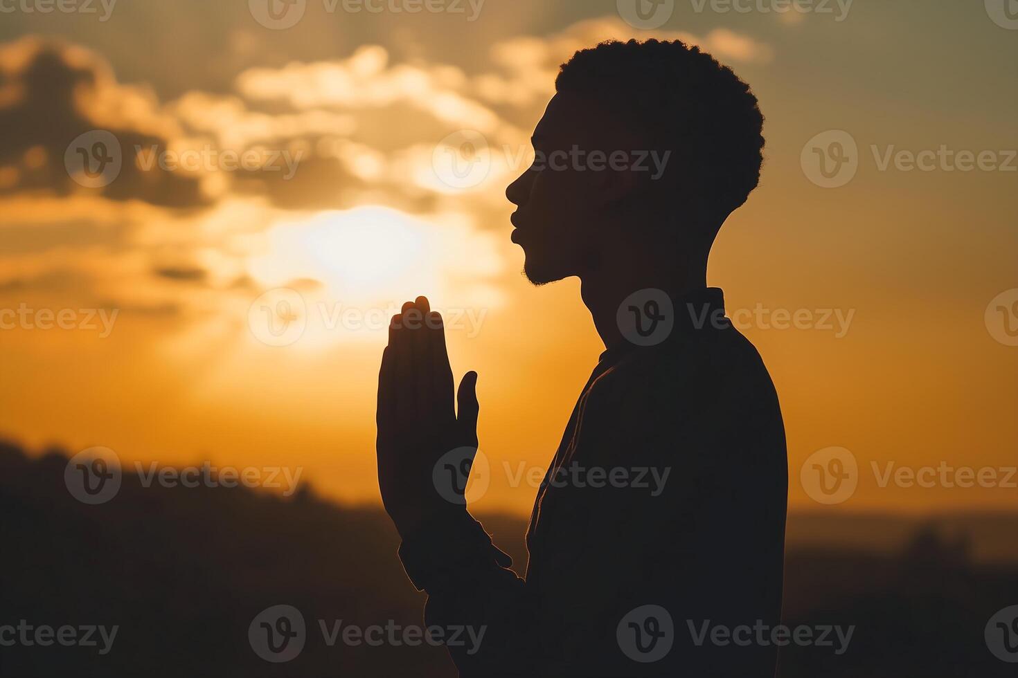 silhouette of a man praying is set against the backdrop of a vibrant sunset photo