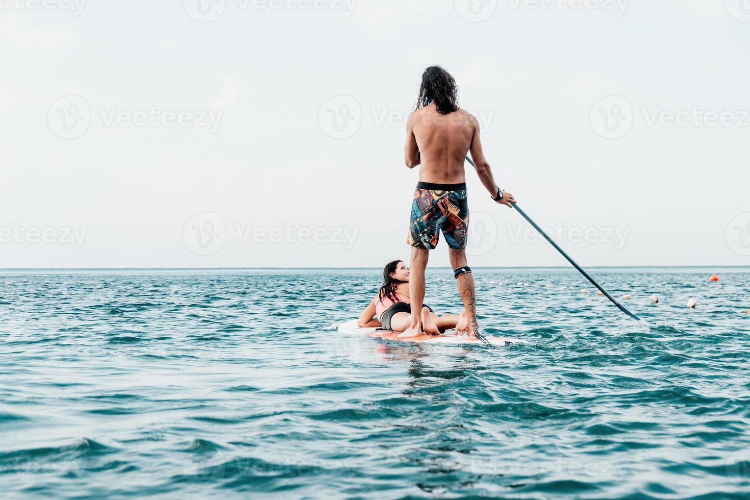 Sea woman and man on sup. Silhouette of happy young woman and man, surfing on SUP board, confident paddling through water surface. Idyllic sunset. Active lifestyle at sea or river. Slow motion photo