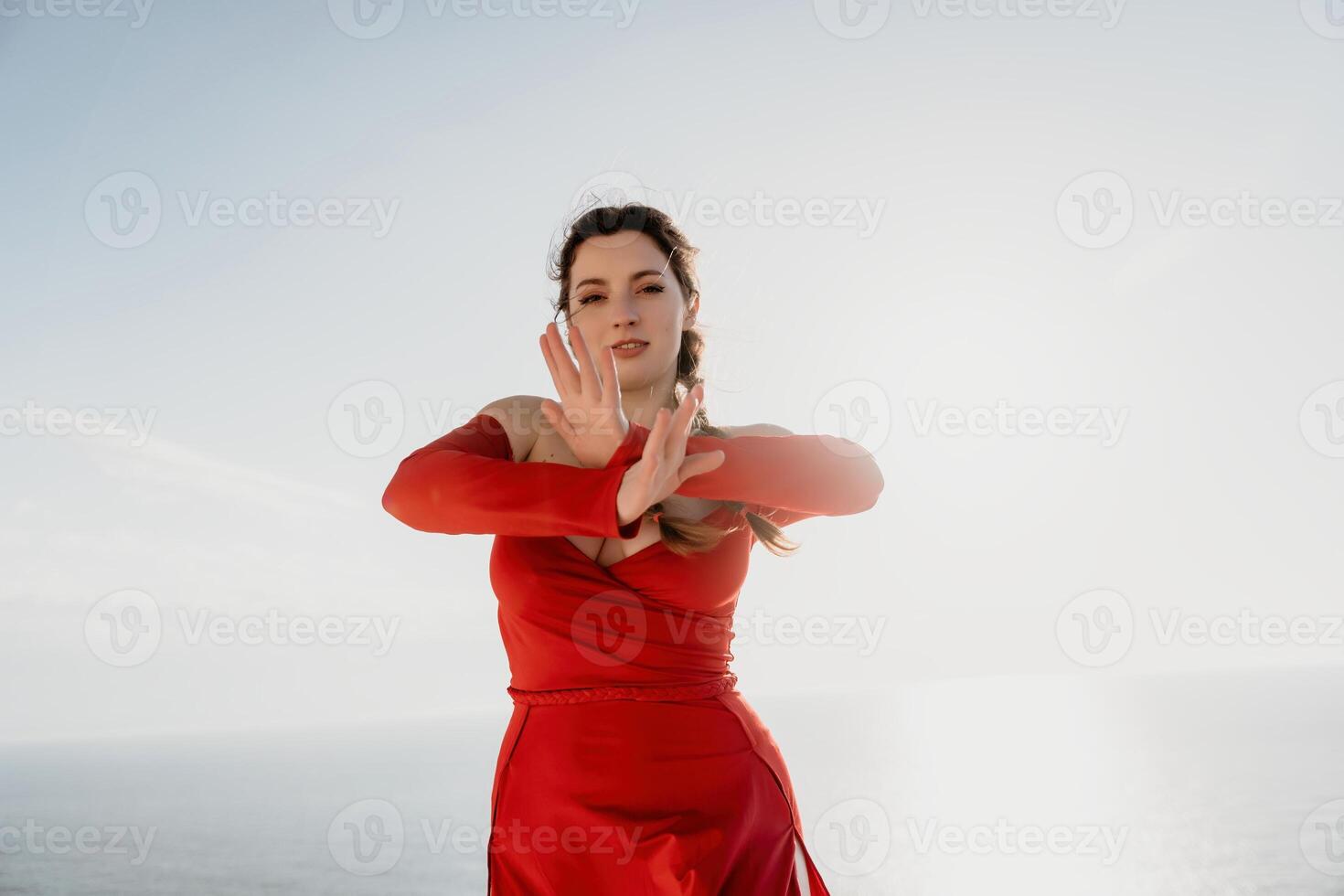 Closeup portrait of sensual young brunette woman in red dress, happily dancing outdoors isolated on blurry sea background with natural bokeh in soft warm sunset backlight. Selective focus. photo