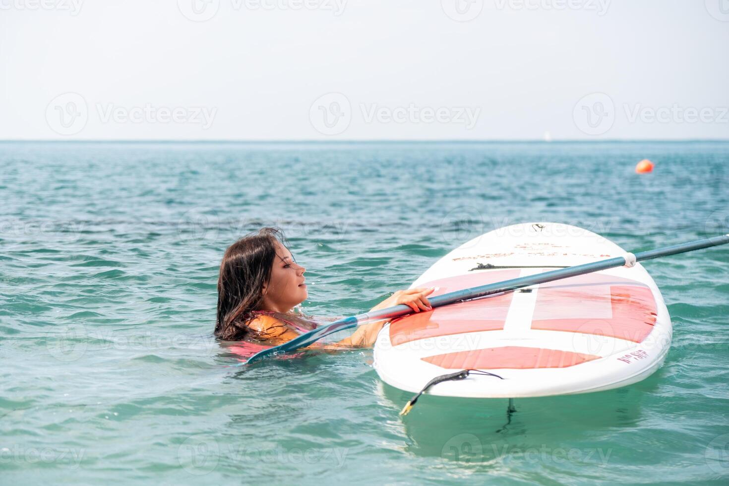 Sea woman sup. Silhouette of happy young woman in pink bikini, surfing on SUP board, confident paddling through water surface. Idyllic sunset. Active lifestyle at sea or river photo