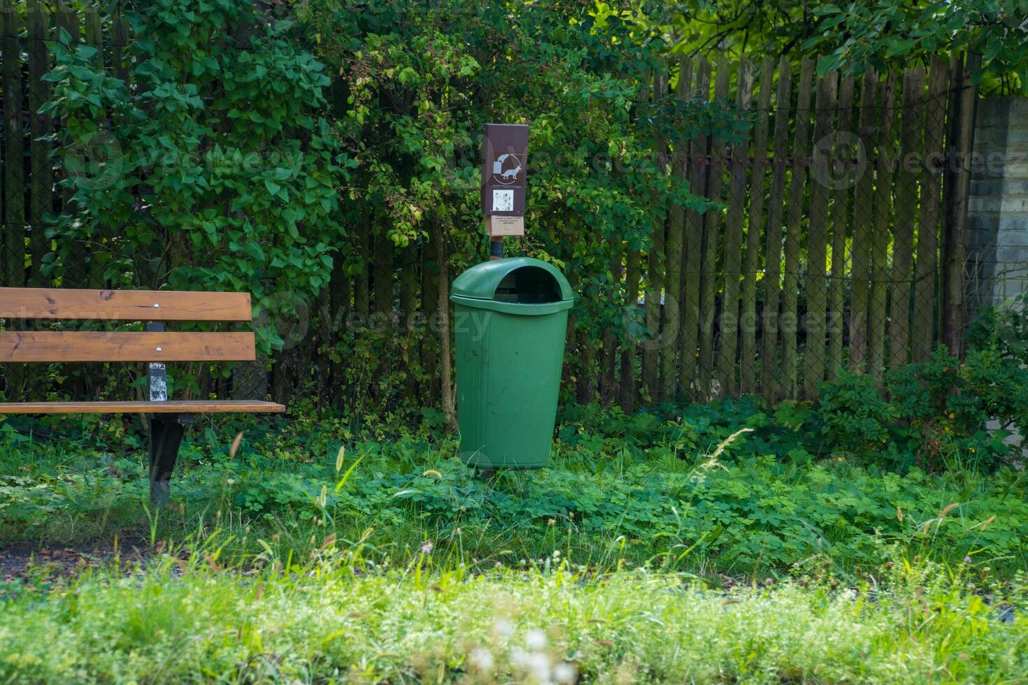 A modern wooden bench with trash bin standing . garbage can with bags for dogs photo