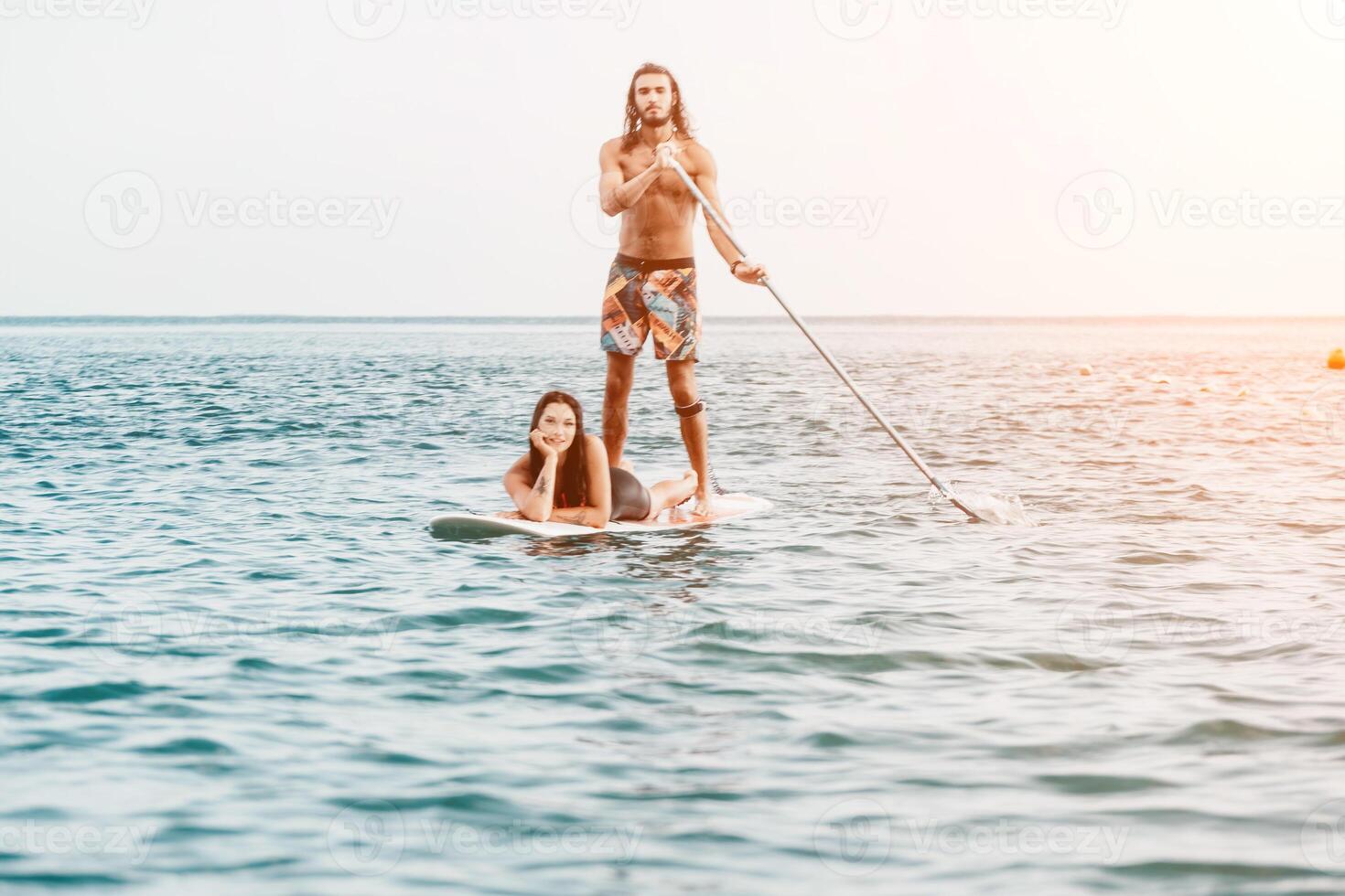 Sea woman and man on sup. Silhouette of happy young woman and man, surfing on SUP board, confident paddling through water surface. Idyllic sunset. Active lifestyle at sea or river. Slow motion photo