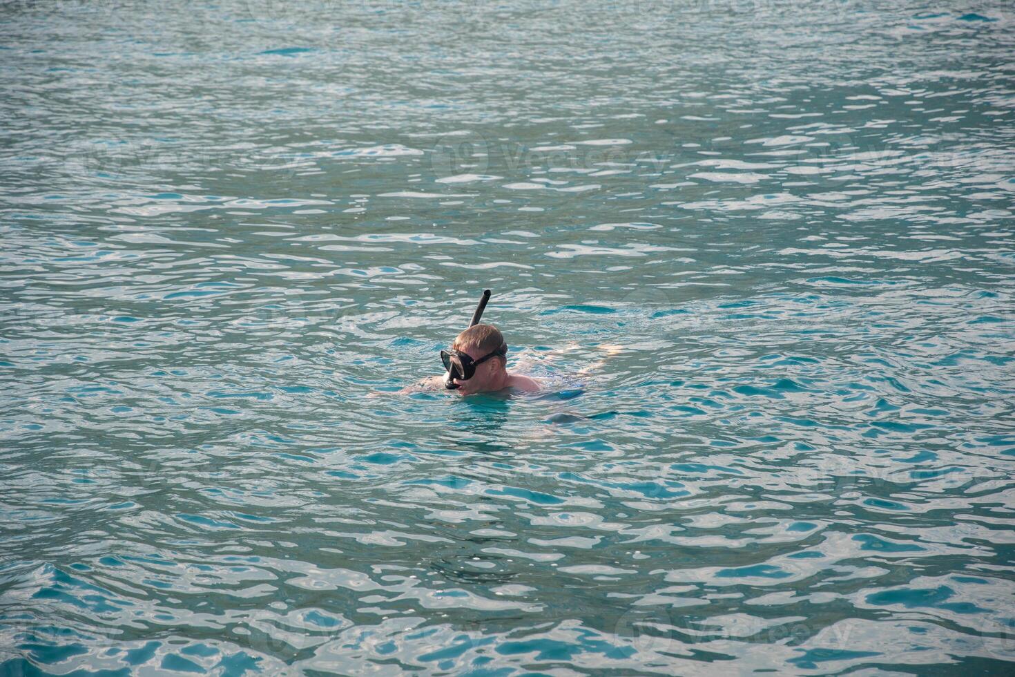 Active young guy in diving mask enjoying swimming in refreshing clear sea water on sunny day, scuba diving concept in turquoise sea, photo