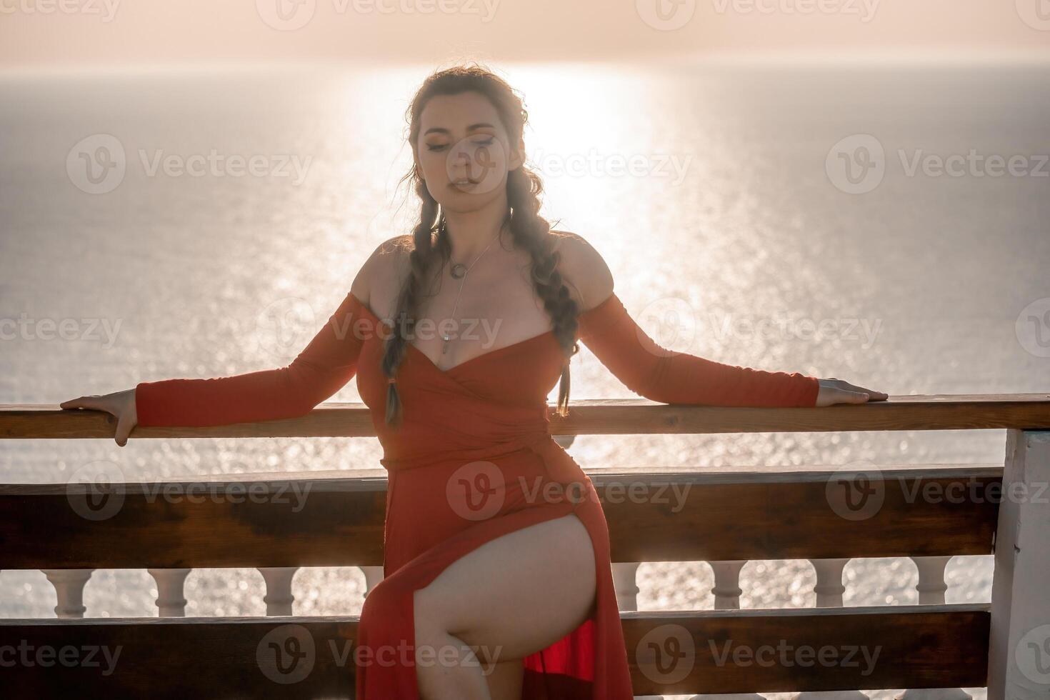 Closeup portrait of sensual young brunette woman in red dress, happily dancing outdoors isolated on blurry sea background with natural bokeh in soft warm sunset backlight. Selective focus. photo