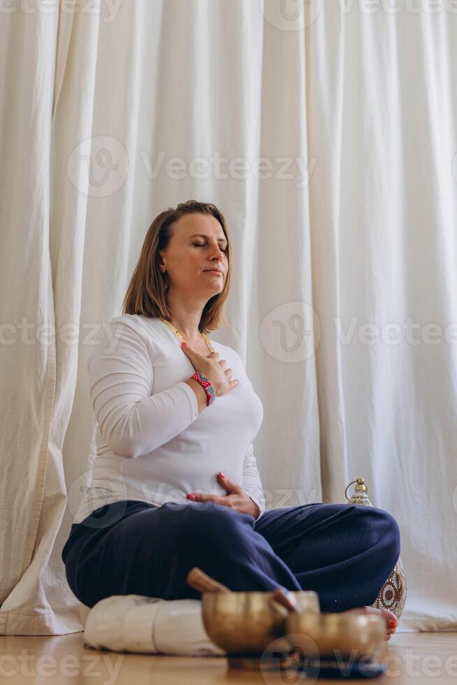 A woman sits on the floor with her eyes closed, practicing deep breathing exercises. She inhales and exhales slowly photo