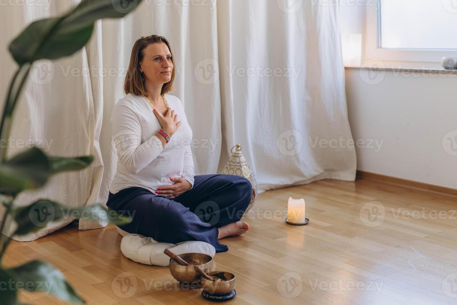 A woman sits on the floor with her eyes closed, practicing deep breathing exercises. She inhales and exhales slowly photo