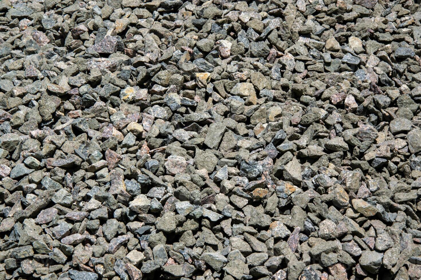 A close-up of grey gravel rocks on a sunny day. The rocks are various sizes and shapes, and they are spread out evenly across the frame photo