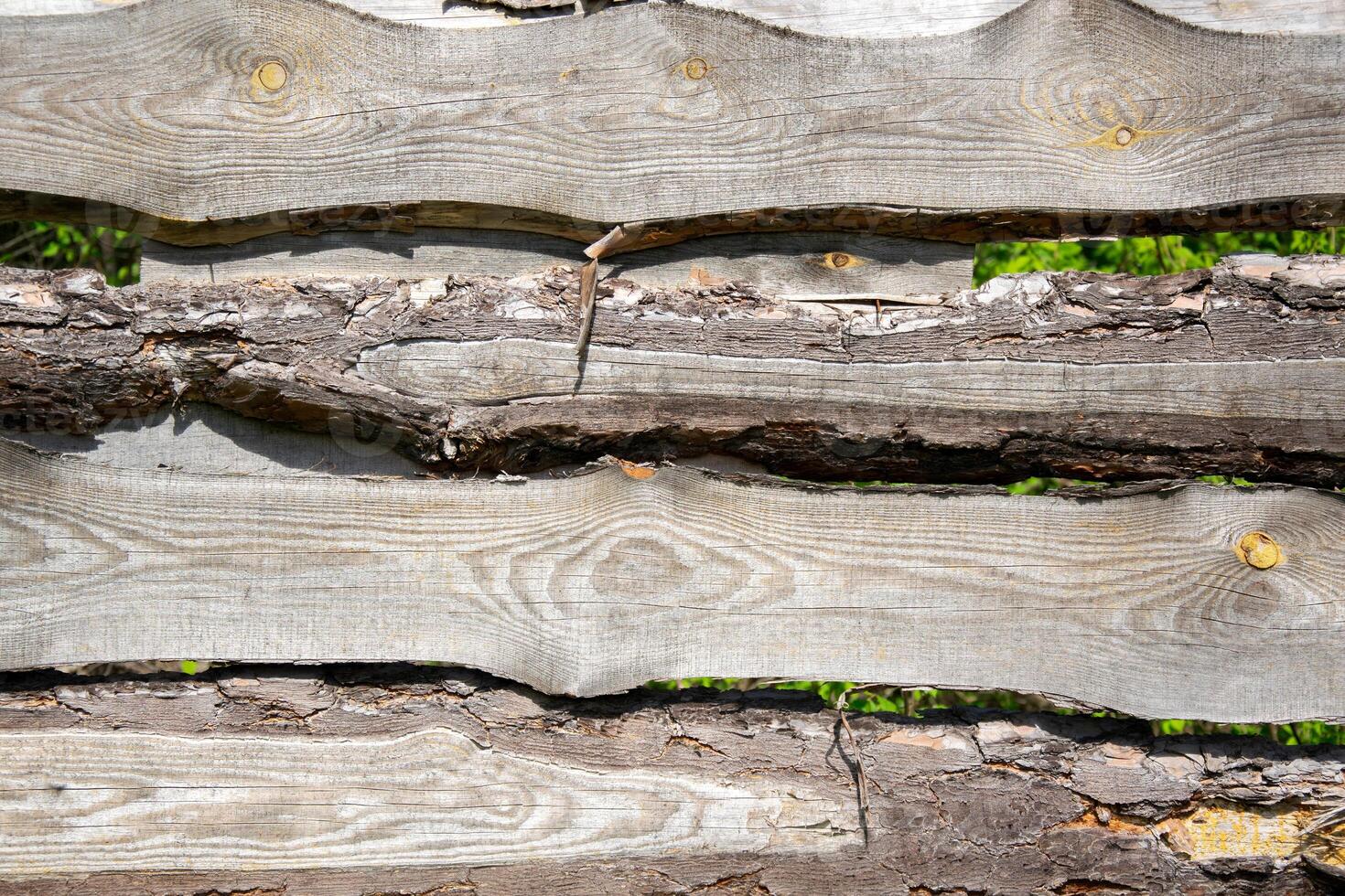 A close-up photo of a weathered wooden fence with visible knots and grain patterns