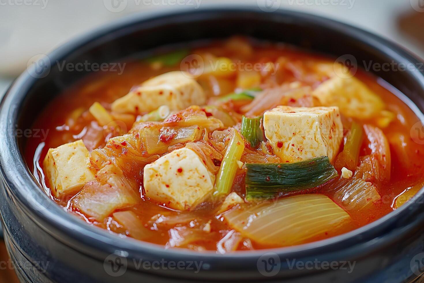 Korean kimchi soup with soft tofu served in a traditional black stone bowl. photo