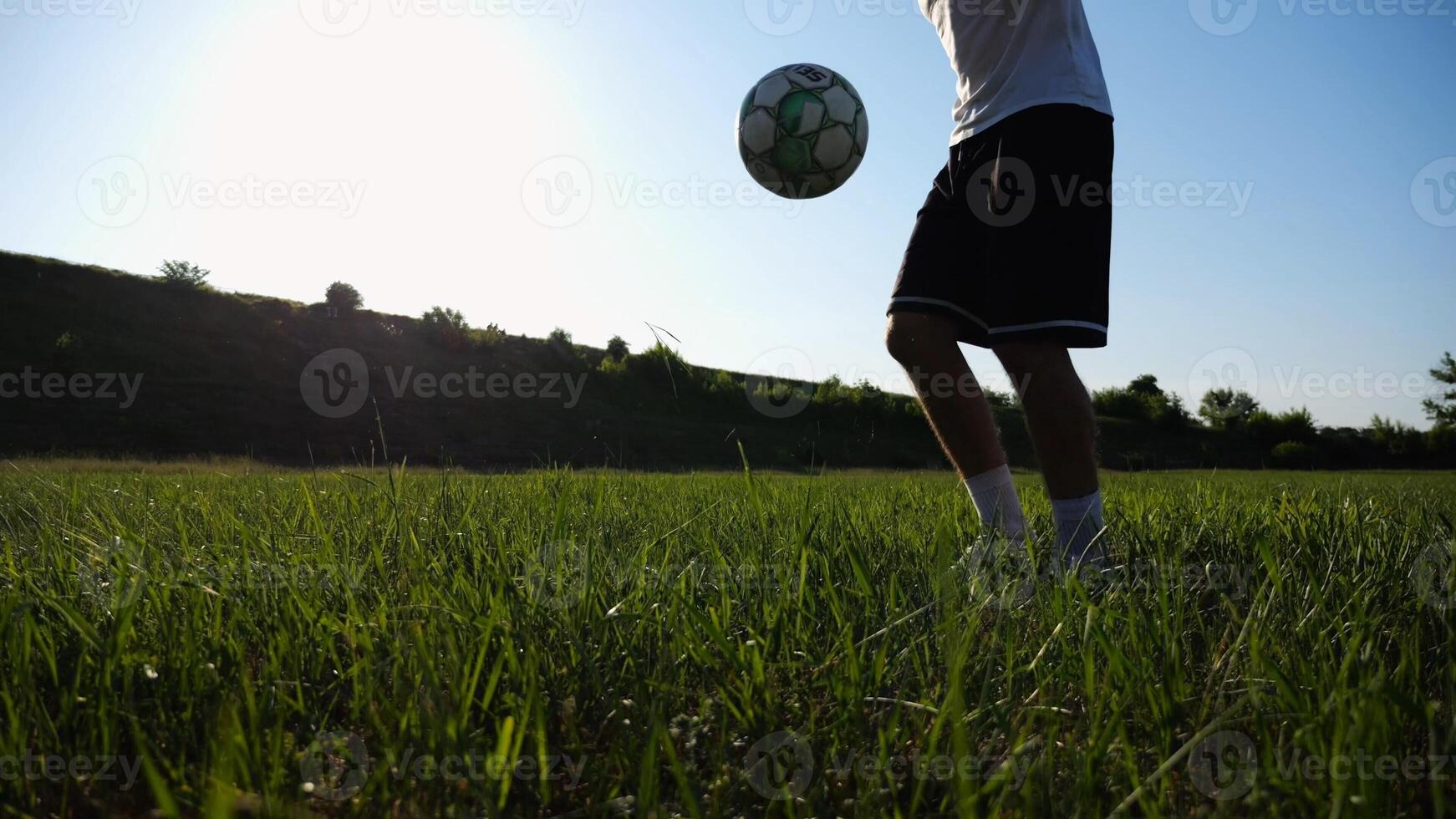Sportsman juggling soccer ball on stadium at sunny day. Young man kicking ball at green field. Professional footballer practicing tricks at meadow with sunlight at background. Freestyle football. photo