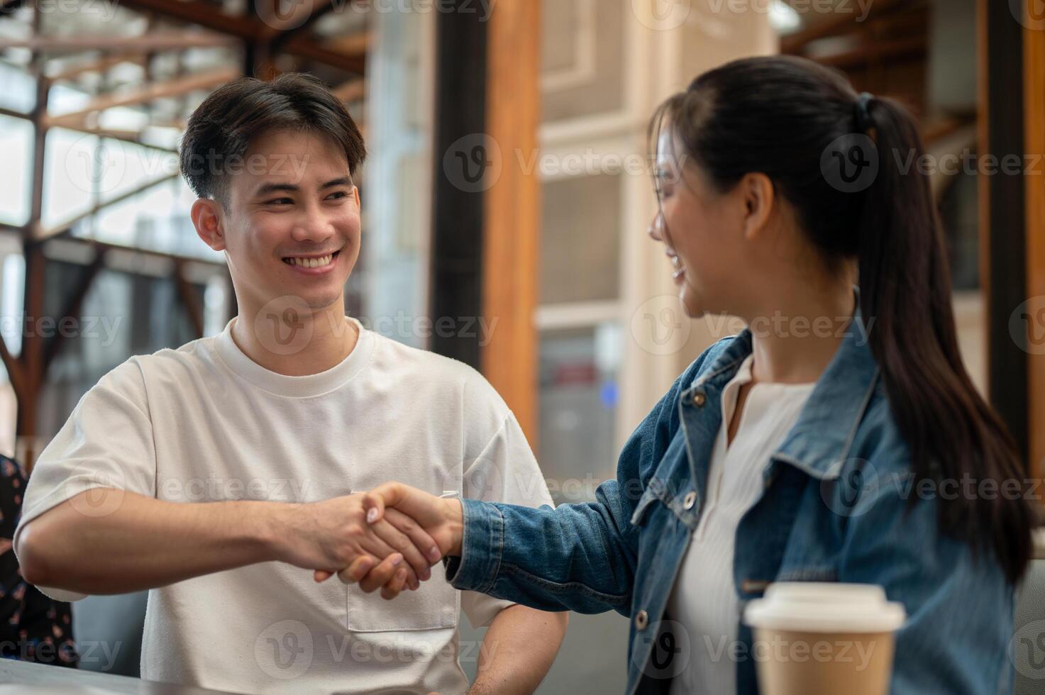 A handsome, cheerful Asian man is shaking hands with his female colleague. photo