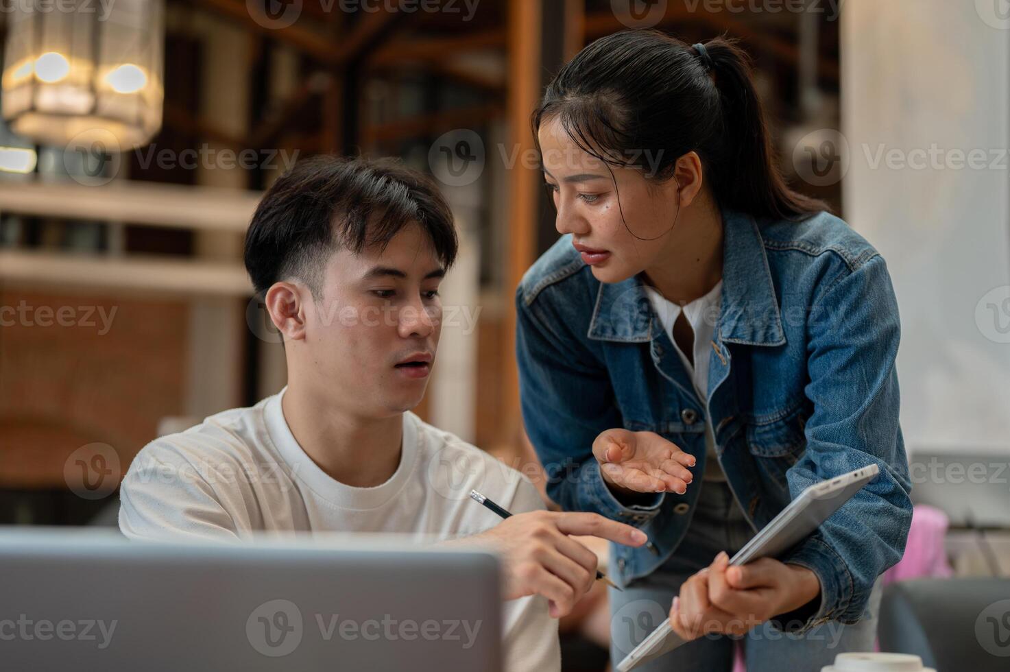 Two Asian friends or colleagues are in a coffee shop, discussing a project while working together. photo