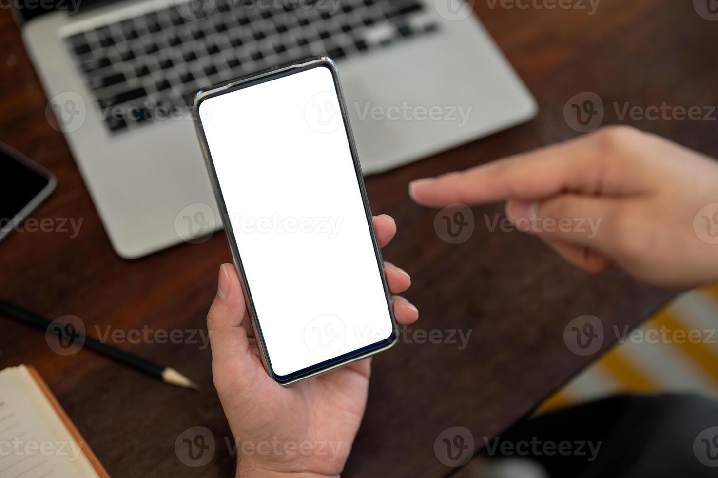 A top view of a man holding a smartphone with a white screen mockup above a desk. photo