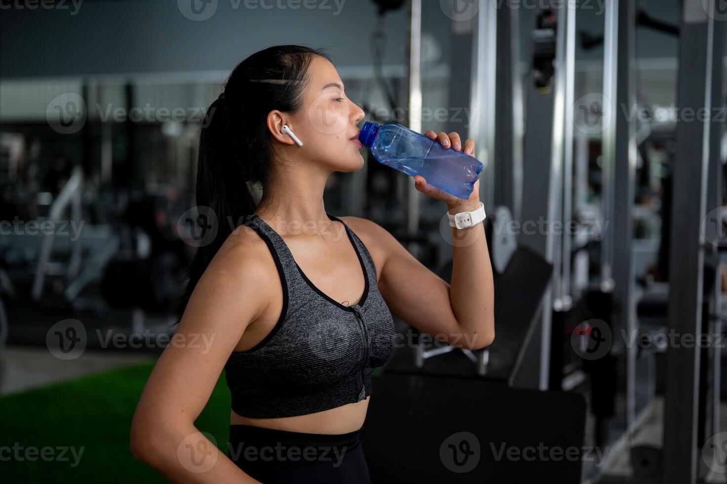 A sporty Asian woman drinking water from a bottle to refresh herself after a workout in the gym. photo