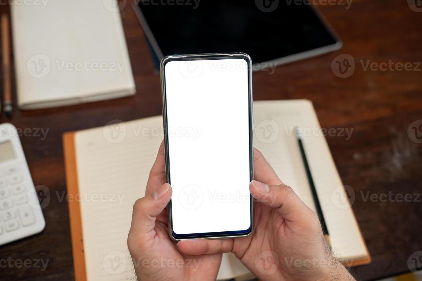 A top view of a man holding a smartphone with a white screen mockup above a desk. photo
