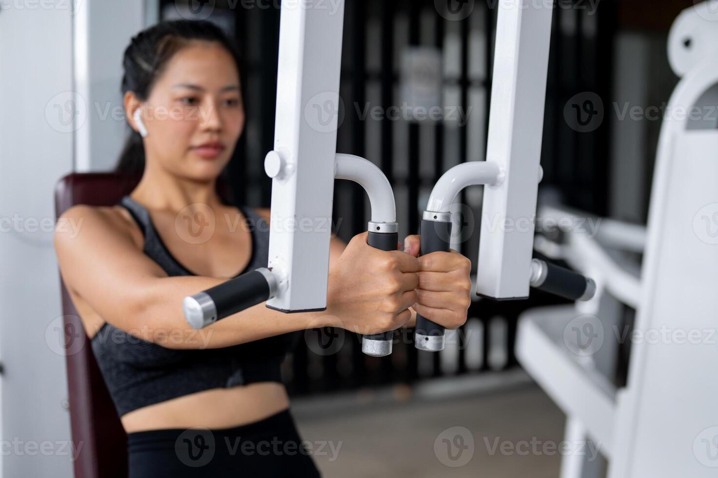 A beautiful, sporty Asian woman in sportswear is training her arms with a machine in the gym. photo