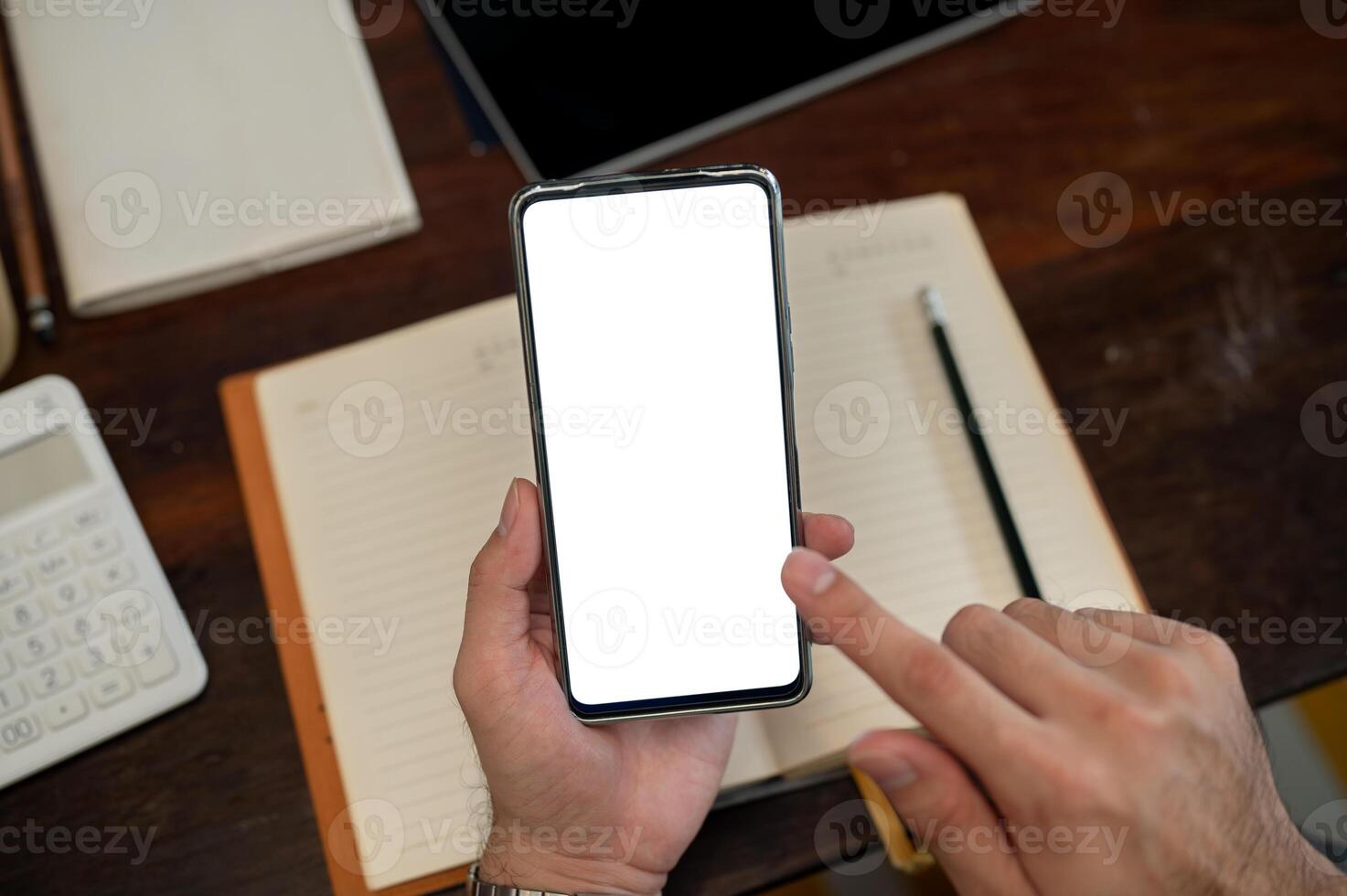 A top view of a man holding a smartphone with a white screen mockup above a desk. photo