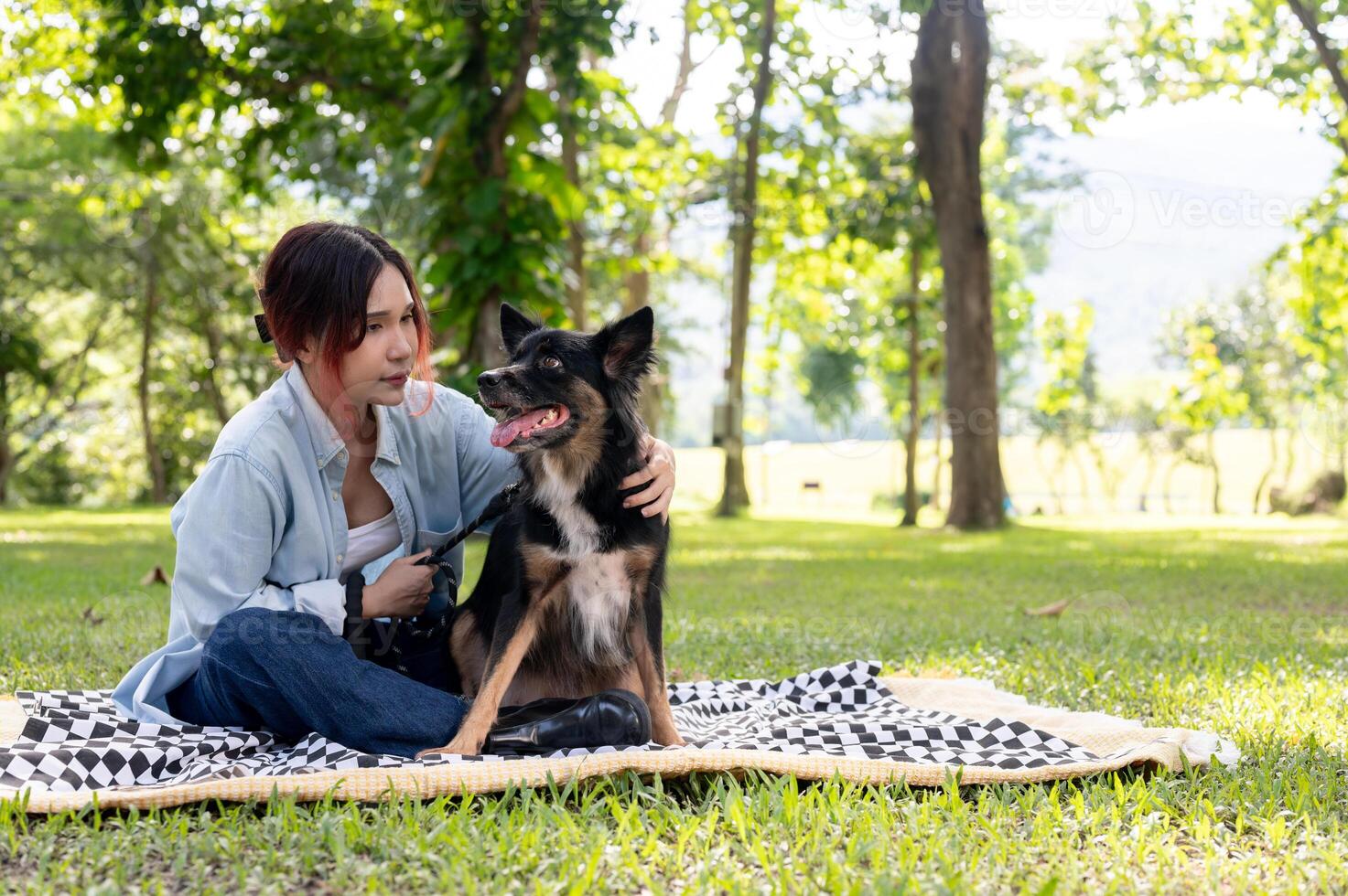 An Asian woman is hanging out with her dog in a green park, sitting together on a picnic cloth. photo