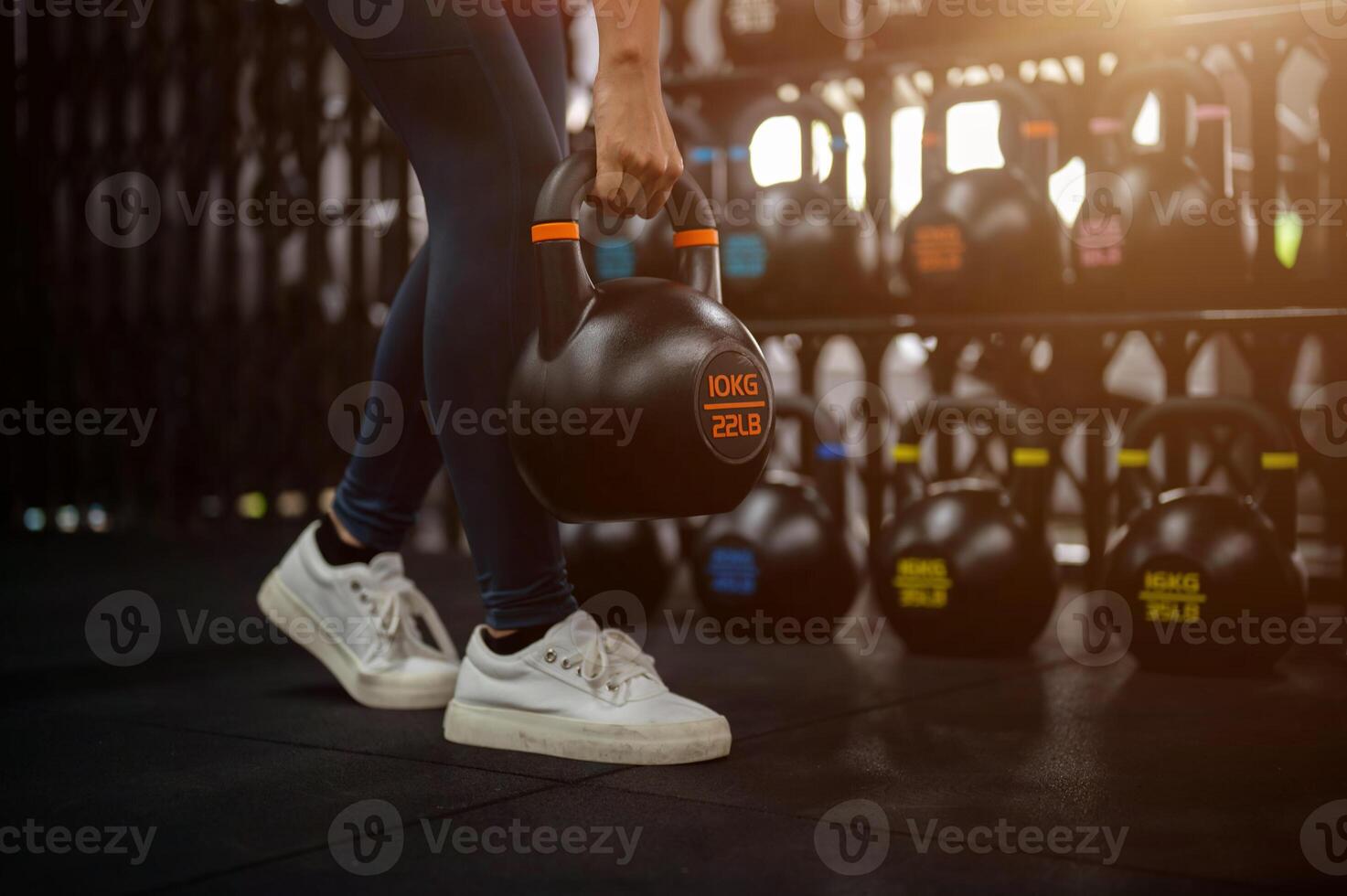 A cropped image of a sporty woman exercising with a kettlebell in the gym, training her glutes. photo