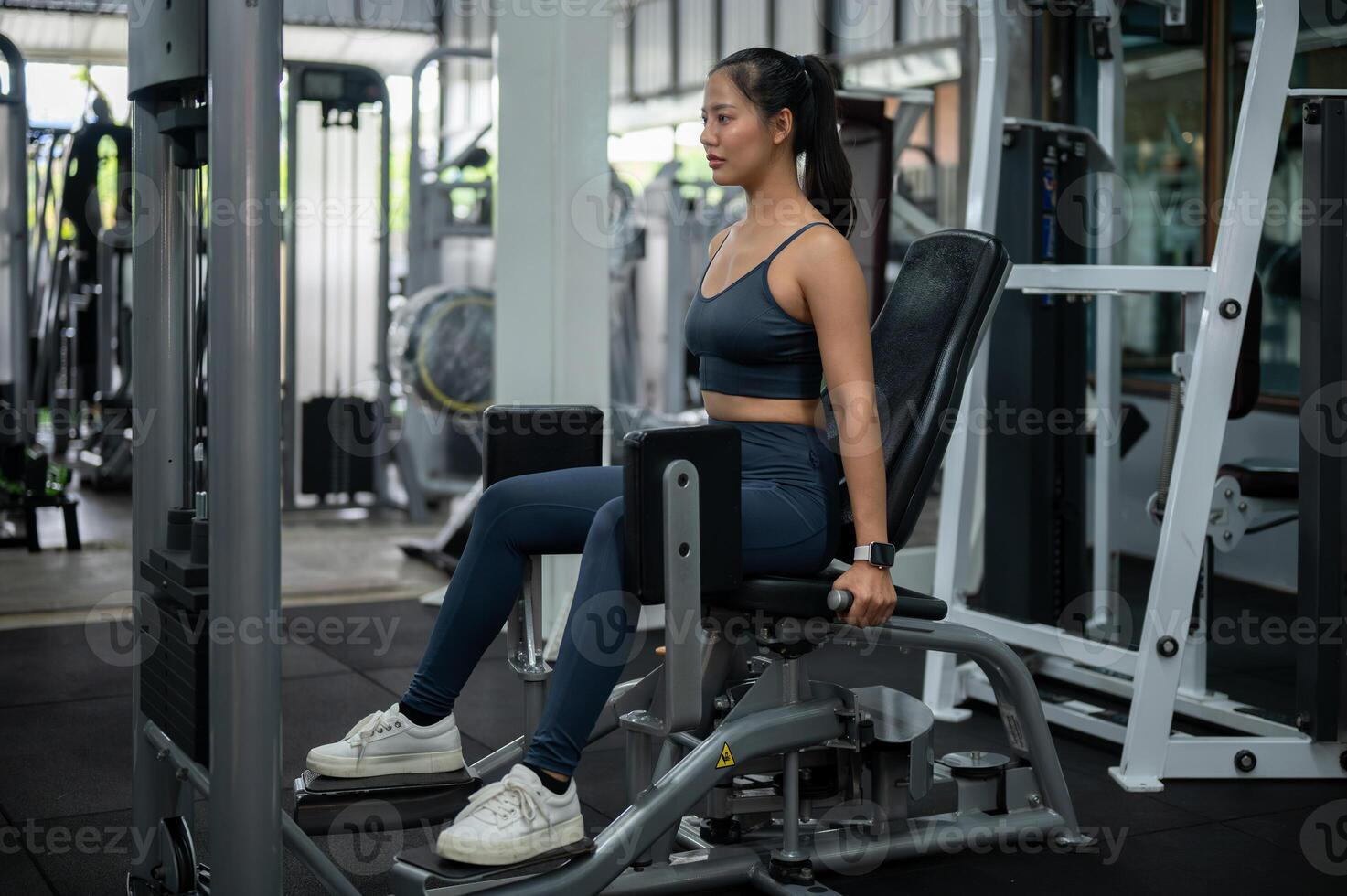 A sporty Asian woman in sportswear is exercising on a hip abduction, adduction machine in the gym. photo
