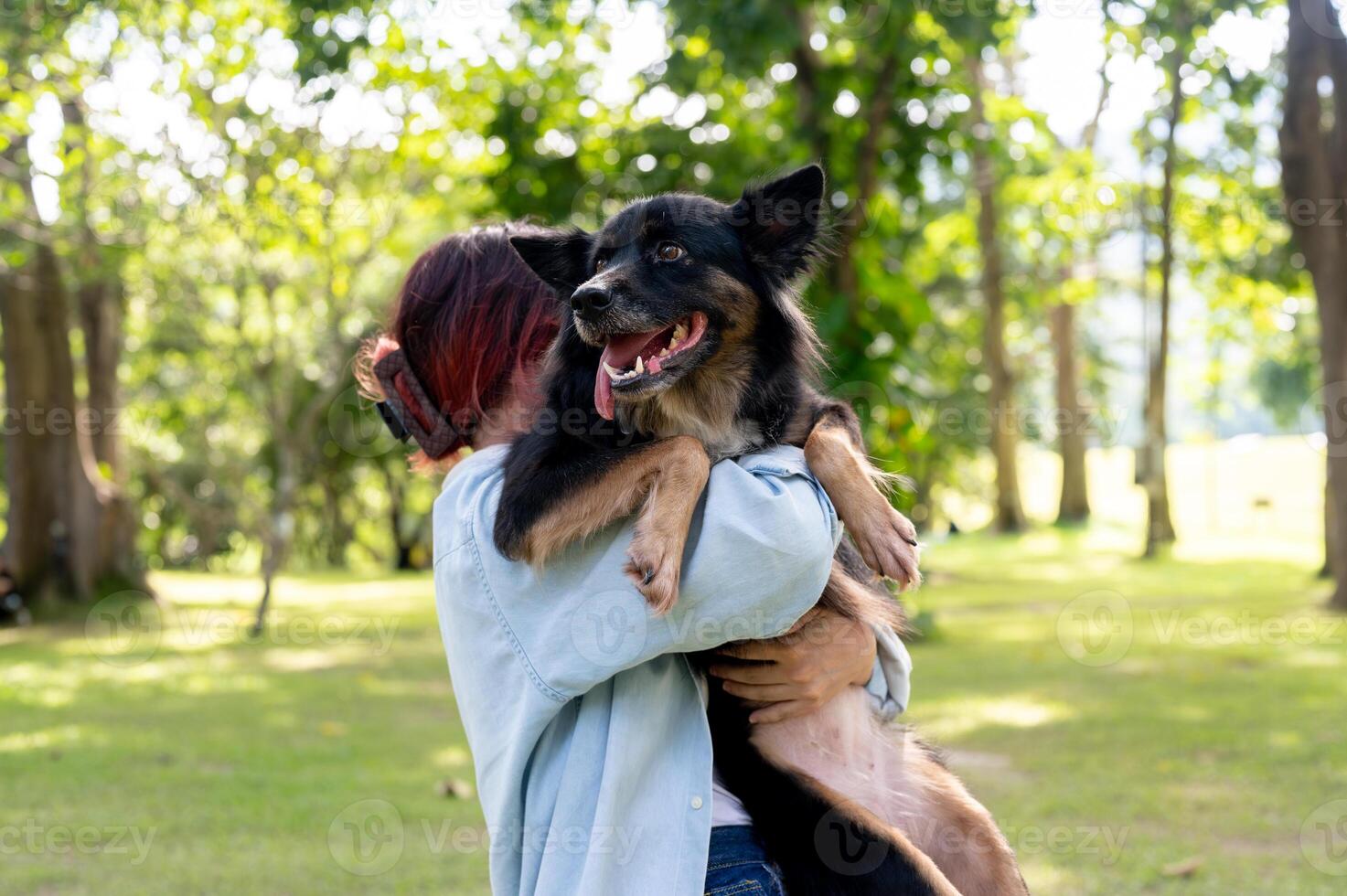 A woman holding her dog in her arms while walking through a green park, hugging her pet. photo