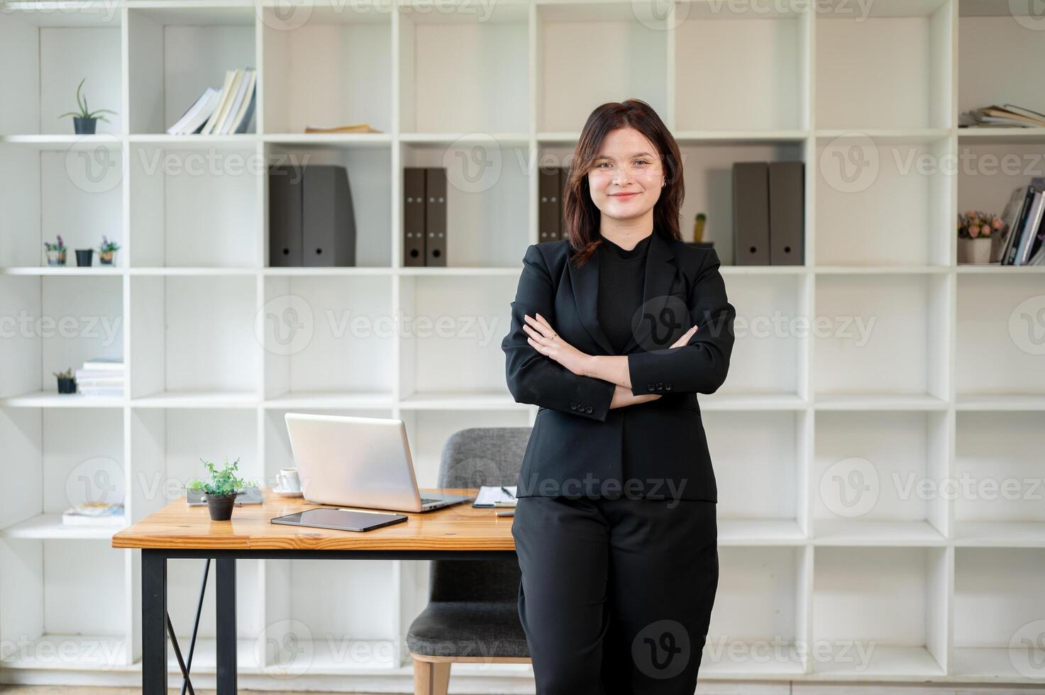 A confident businesswoman standing in her office with her arms crossed, looking at the camera. photo