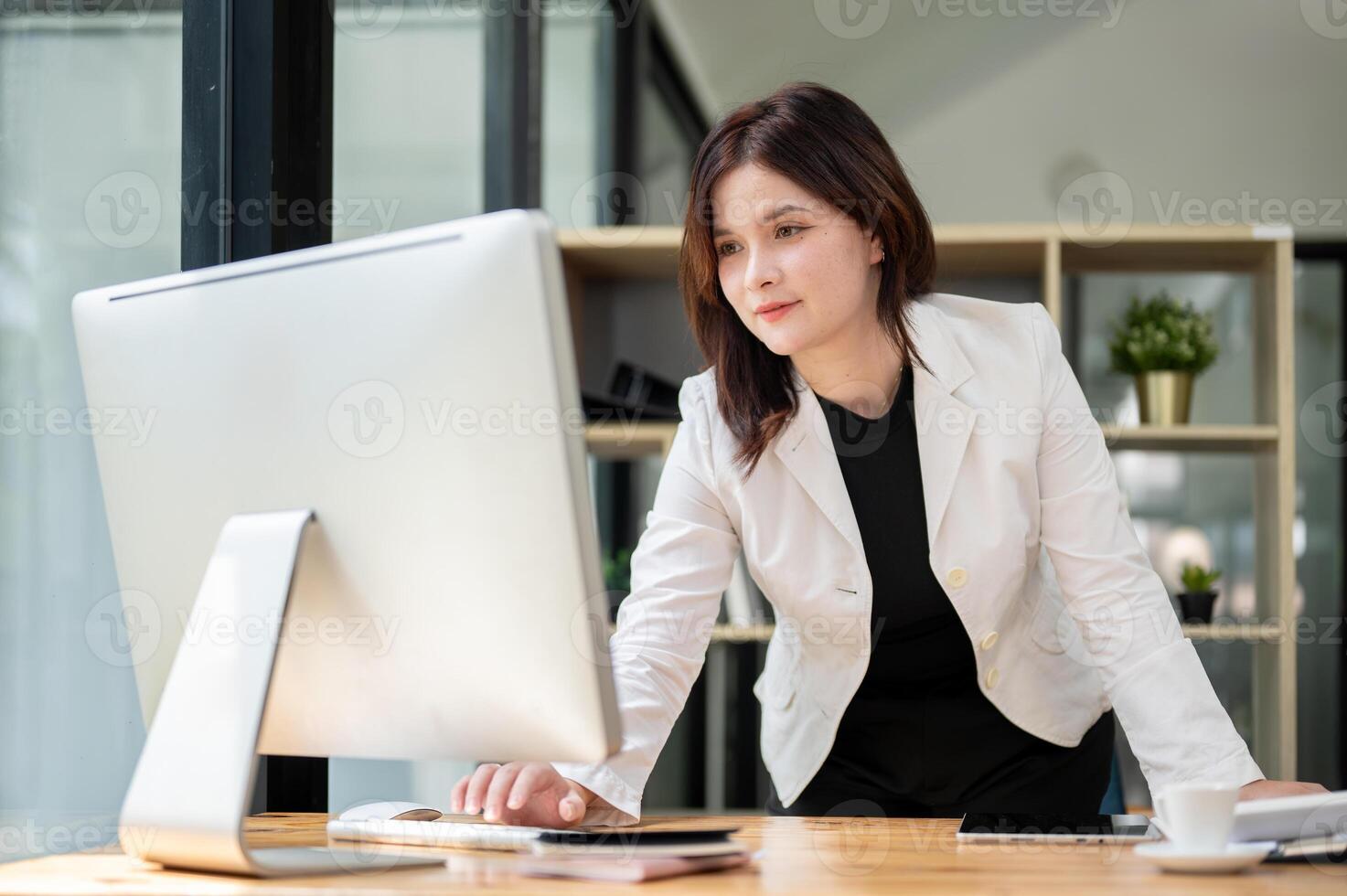 A businesswoman is standing at her desk, typing on a computer keyboard and looking at the screen. photo