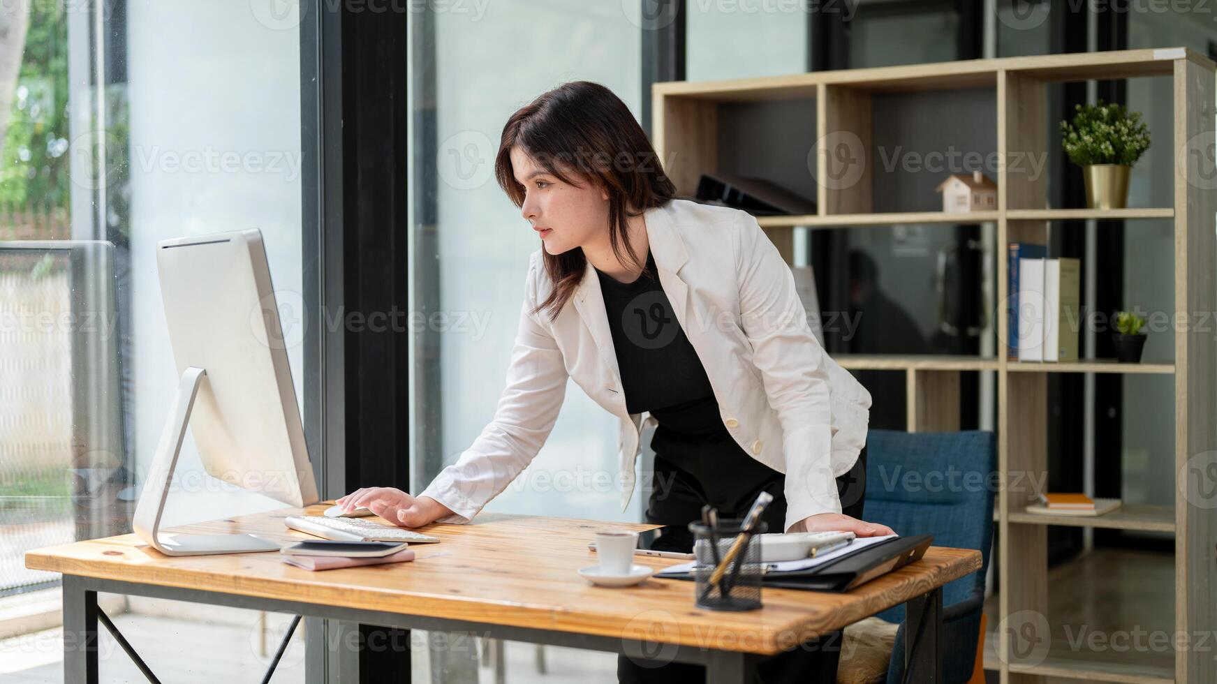 A businesswoman is standing at her desk, typing on a computer keyboard and looking at the screen. photo