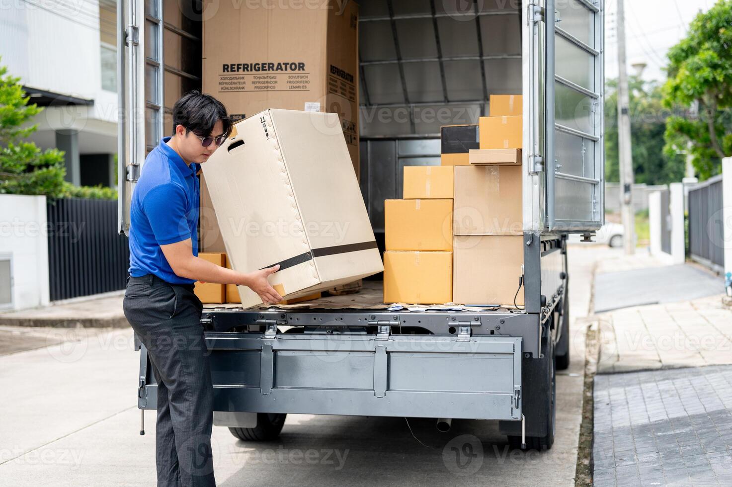 An Asian delivery man or mover is unloading cardboard boxes from his truck. photo