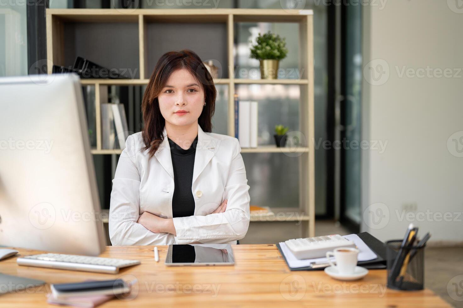 A confident Caucasian businesswoman sitting at her desk in the office with her arms crossed. photo