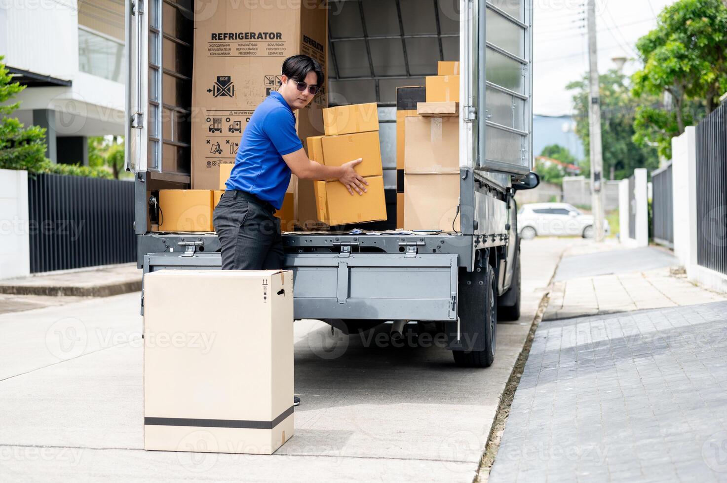An Asian delivery man or mover is unloading cardboard boxes from his truck. photo