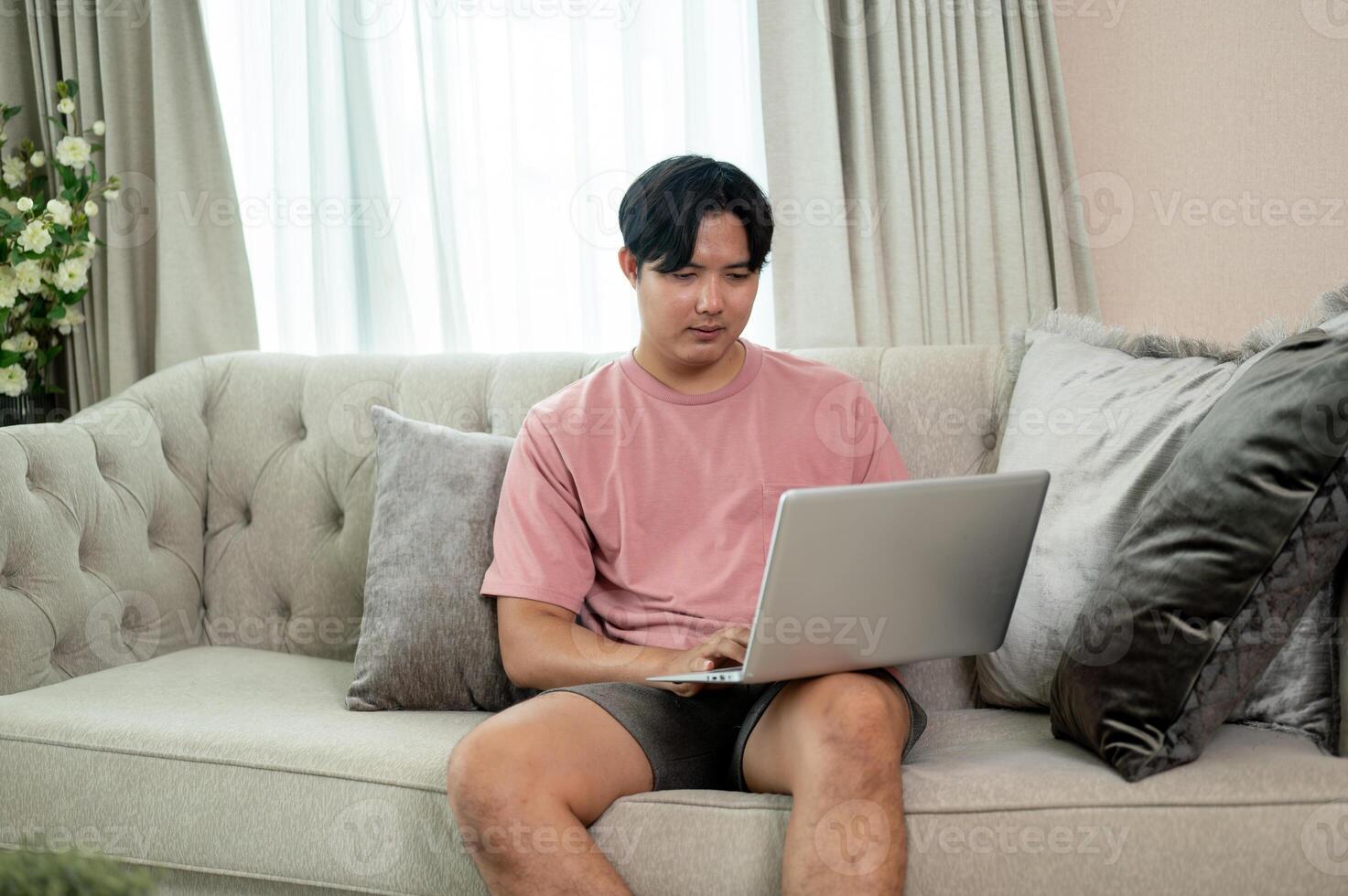 An Asian man in casual clothes using his laptop on a couch in the living room. photo