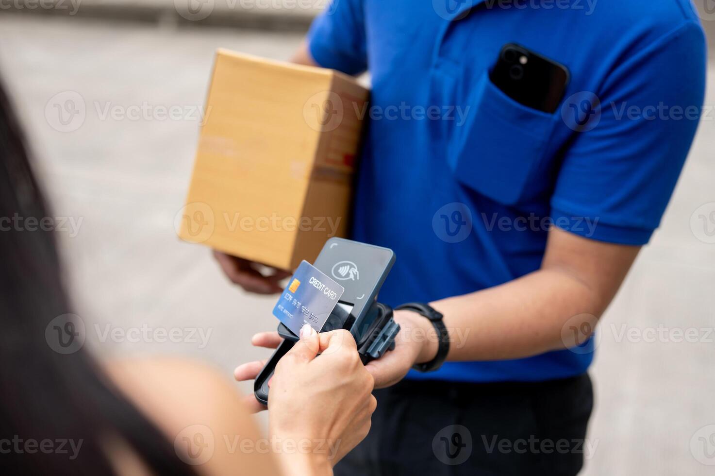 A customer tapping her credit card on a card reader before receiving a package from a delivery man. photo