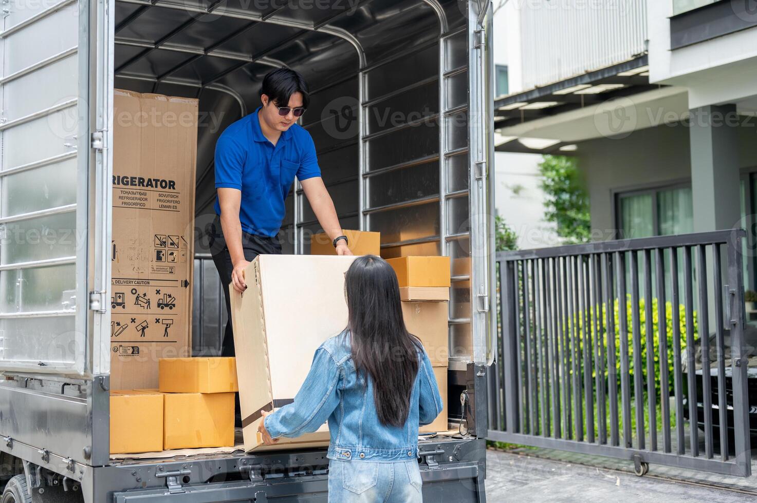 An Asian delivery man is unloading a cardboard box from his truck with his female assistant. photo