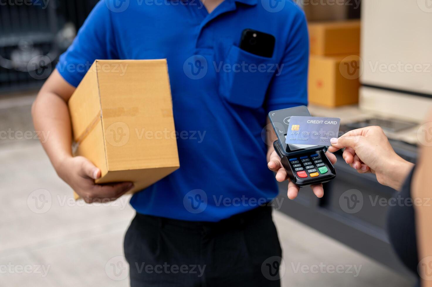A customer tapping her credit card on a card reader before receiving a package from a delivery man. photo