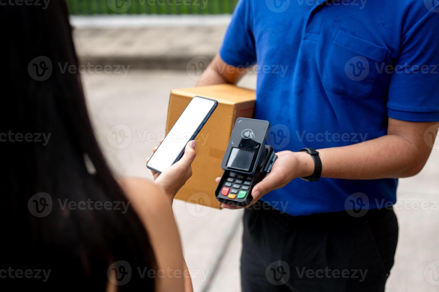 A customer tapping her smartphone on a card reader before receiving a package from a delivery man. photo