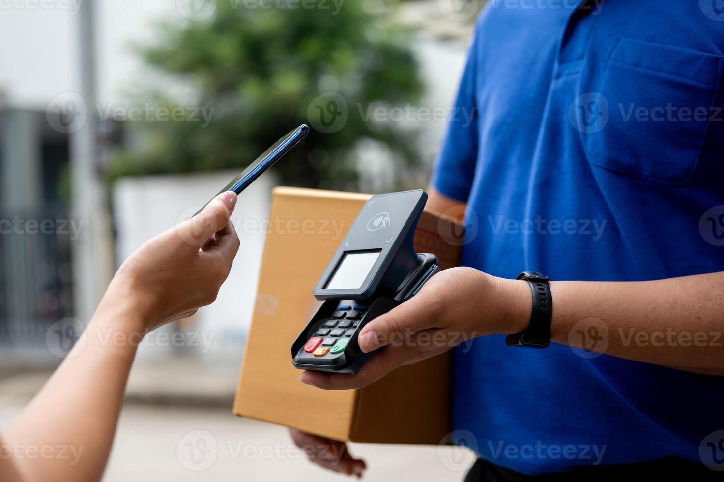 A customer tapping her smartphone on a card reader before receiving a package from a delivery man. photo