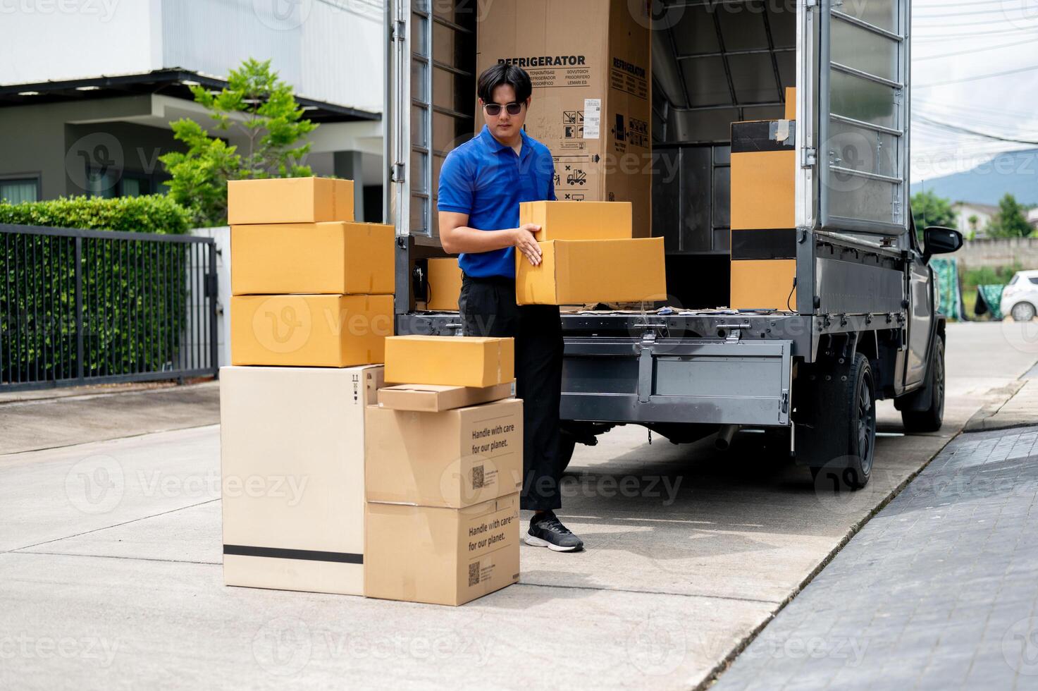 An Asian delivery man or mover is unloading cardboard boxes from his truck. photo