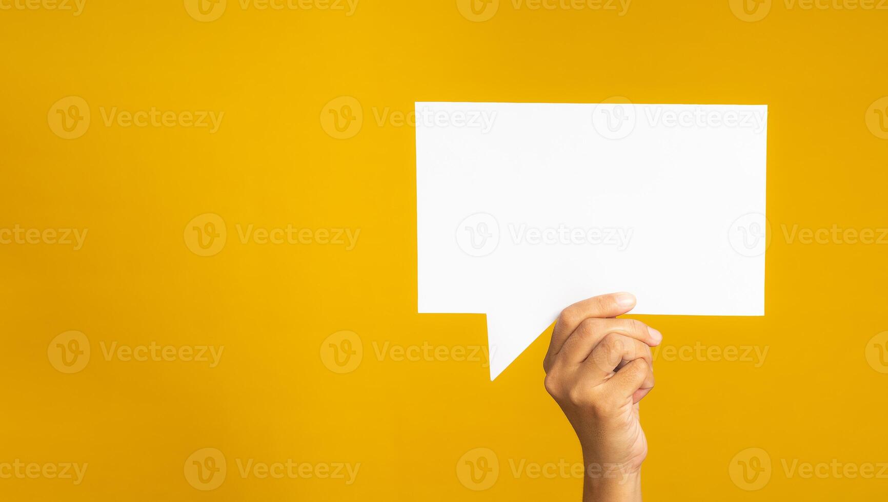 Hand holding of an empty white speech bubble against a yellow background photo