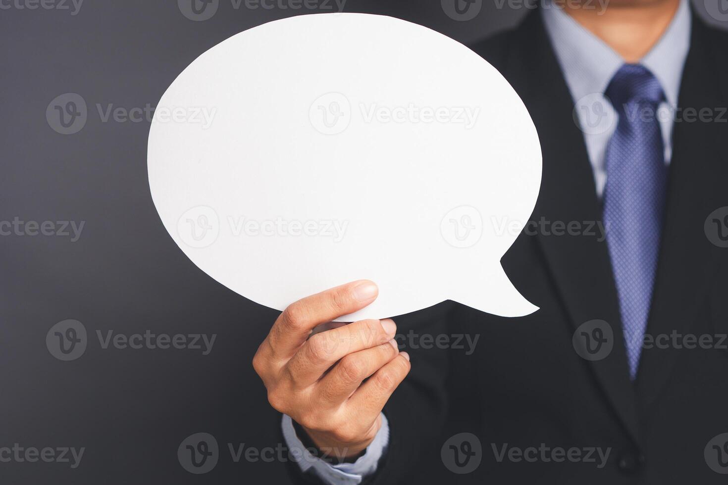 Businessman in suit holding an empty speech bubble standing against a gray background photo