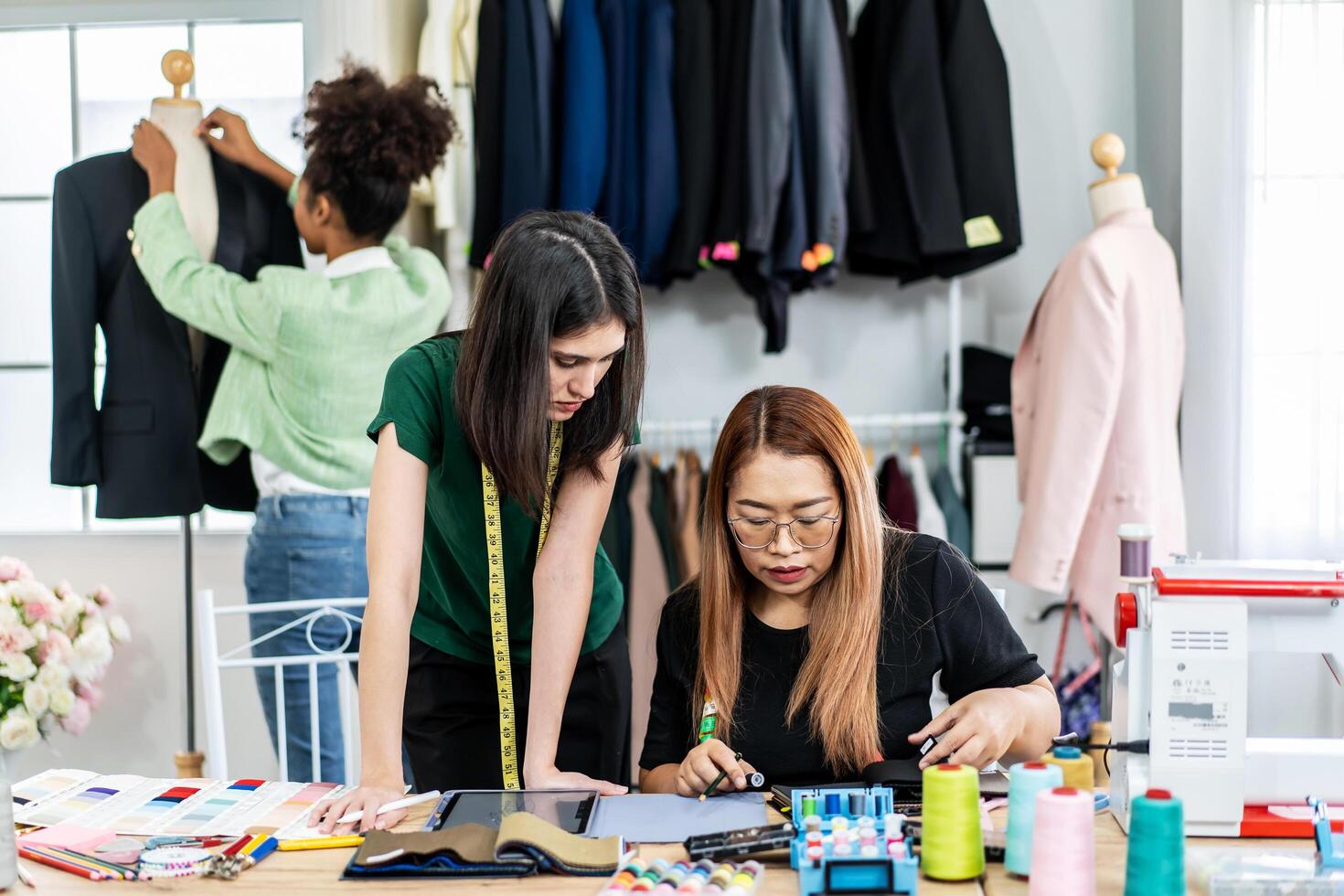 Team of three fashion designers preparation for create new clothes collection in workshop studio and tablet for checking with sample fabric colors, They talking about clothing design at work place. photo